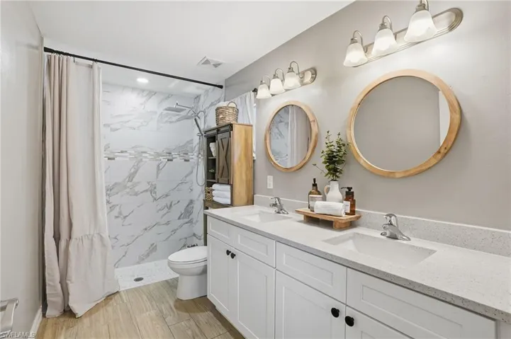 Bathroom featuring a shower stall, double vanity, and light wood-type flooring