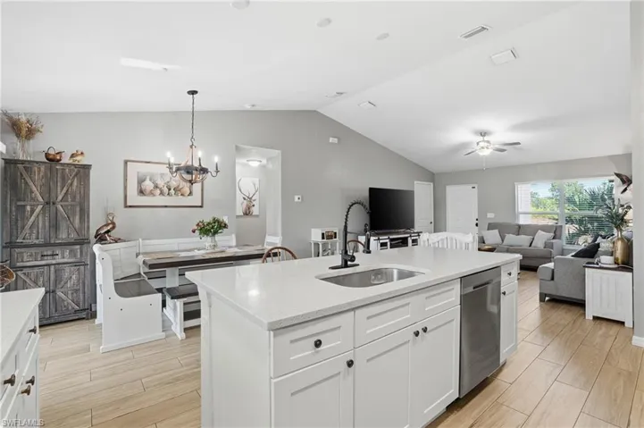 Kitchen with white cabinets, open floor plan, vaulted ceiling, light stone countertops, and hanging light fixtures