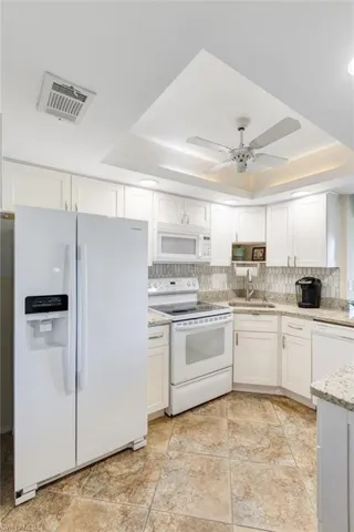 Kitchen featuring a tray ceiling, white appliances, white cabinetry, and backsplash