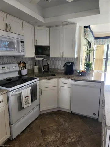 Kitchen with white appliances, white cabinets, and light stone counters