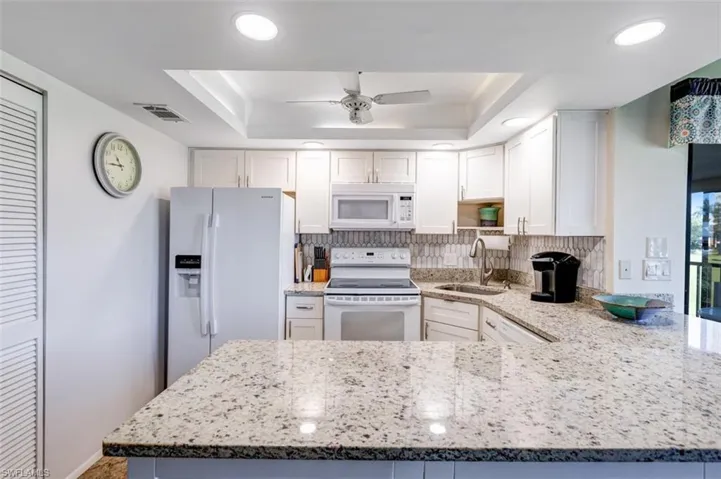 Kitchen featuring white appliances, light stone countertops, white cabinets, and recessed lighting