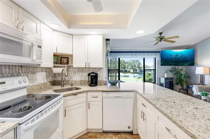 Kitchen with white appliances, a ceiling fan, white cabinetry, light stone counters, and recessed lighting