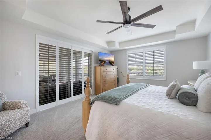 Carpeted bedroom featuring a tray ceiling, multiple windows, and ceiling fan
