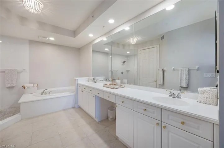 Bathroom featuring a shower stall, double vanity, a garden tub, and a chandelier