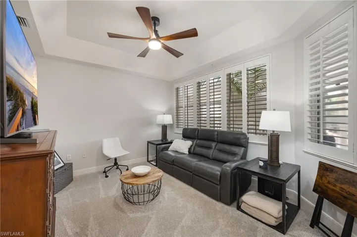 Living area with a raised ceiling, carpet floors, and ceiling fan
