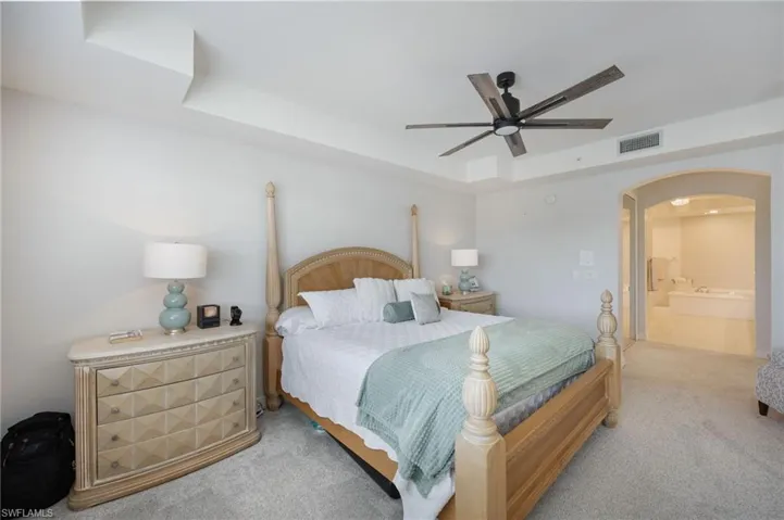 Carpeted bedroom featuring a tray ceiling, a ceiling fan, arched walkways, and connected bathroom