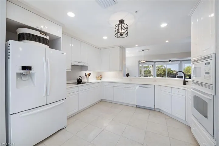 Kitchen featuring white appliances, white cabinets, hanging light fixtures, and light tile patterned floors