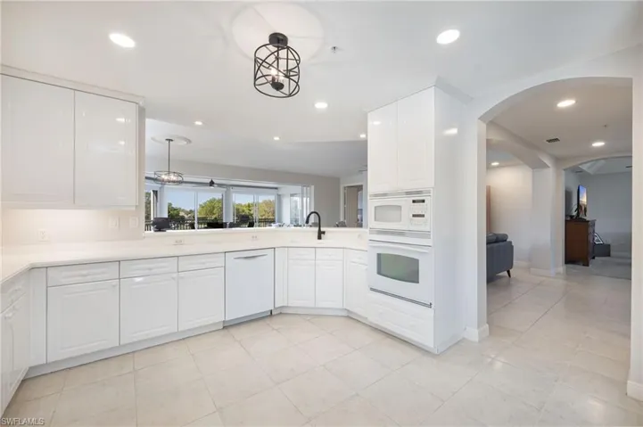 Kitchen with white cabinets, white appliances, recessed lighting, arched walkways, and light tile patterned floors