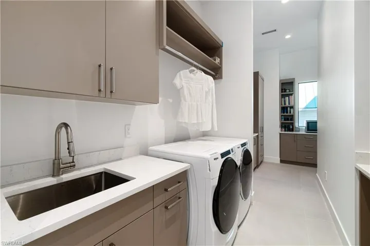 Laundry room with light tile patterned floors, separate washer and dryer, cabinets, and sink