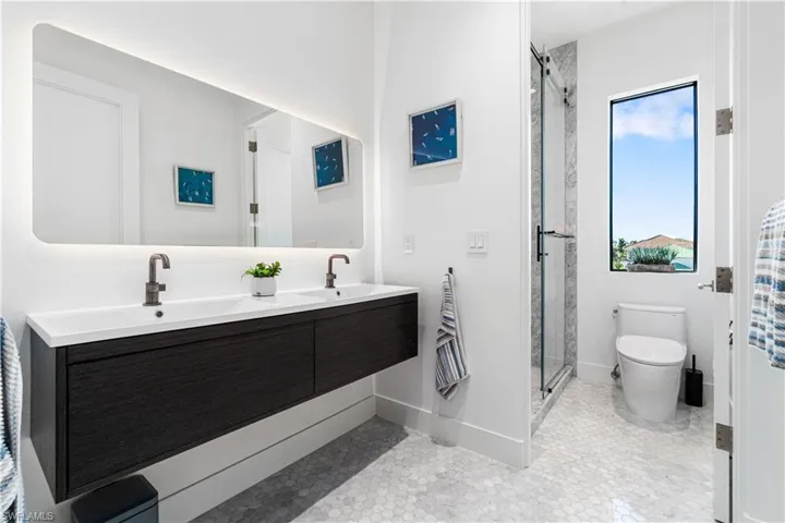 Bathroom with dual vanity, toilet, tile patterned floors, and a shower with shower door