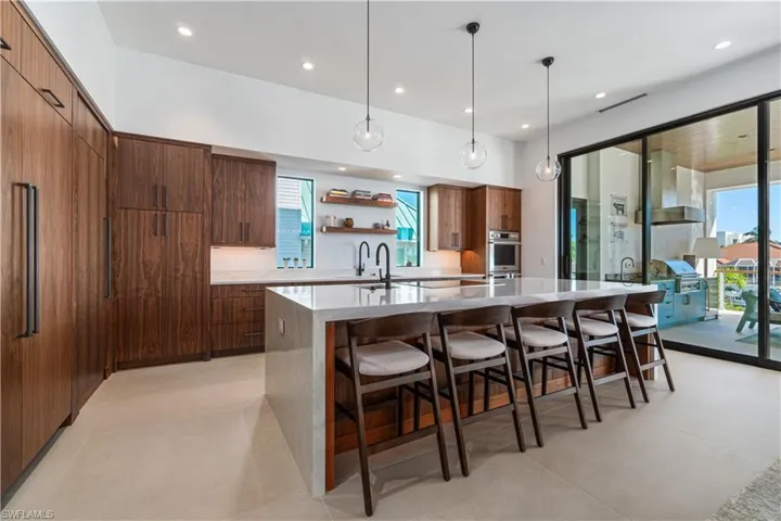 Kitchen with plenty of natural light, stainless steel oven, wall chimney range hood, light tile patterned floors, and an island with sink