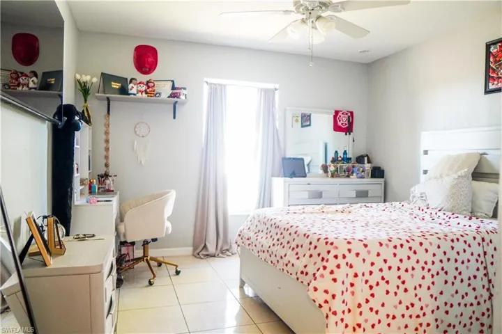 Bedroom with an office area, light tile patterned floors, and ceiling fan