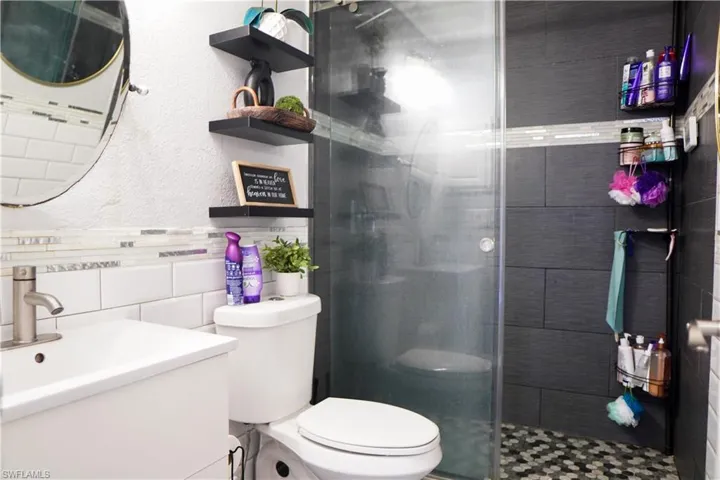 Full bathroom with a textured wall, vanity, tile walls, a shower stall, and tasteful backsplash