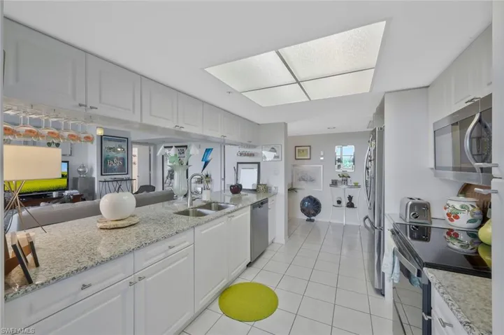 Kitchen featuring appliances with stainless steel finishes, light stone counters, open floor plan, white cabinets, and light tile patterned floors