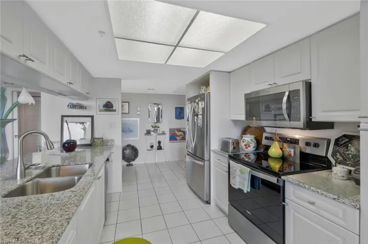 Kitchen with stainless steel appliances, white cabinets, light stone counters, and light tile patterned floors