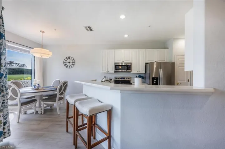 Kitchen with decorative light fixtures, visible vents, appliances with stainless steel finishes, white cabinets, and a kitchen bar