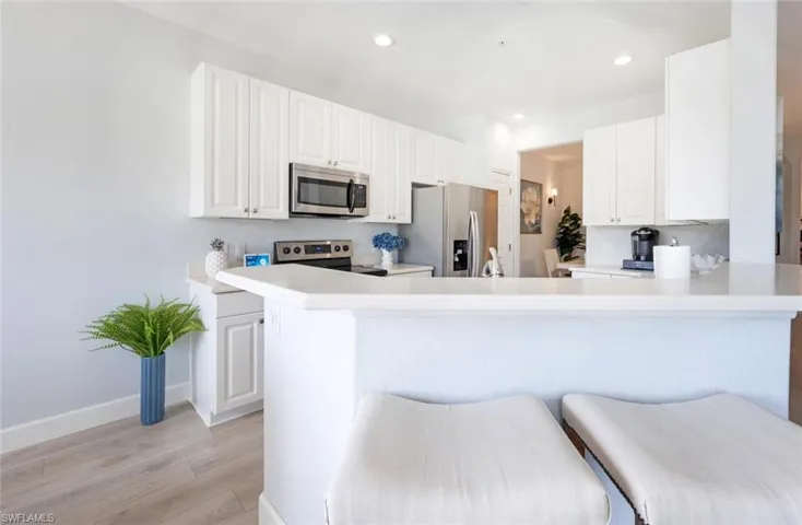 Kitchen featuring light wood finished floors, appliances with stainless steel finishes, a peninsula, light countertops, and a kitchen bar