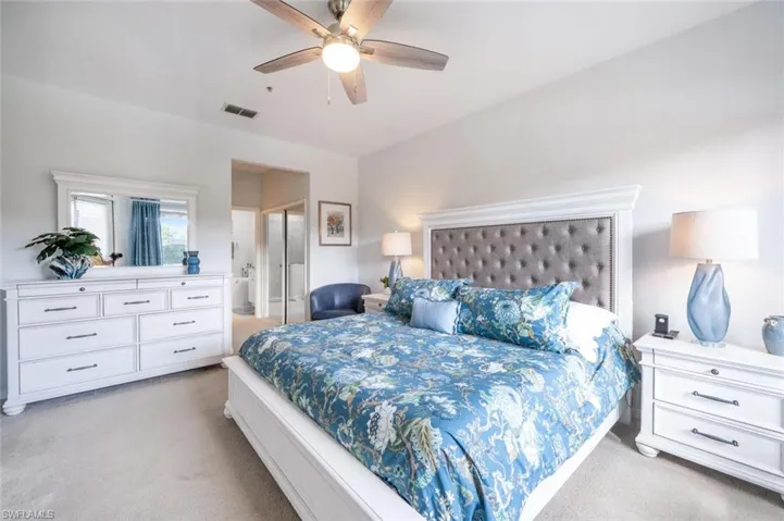 Bedroom with ceiling fan, connected bathroom, visible vents, and light colored carpet
