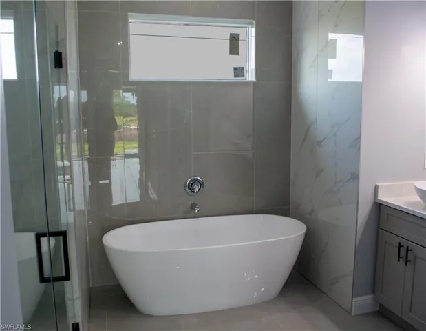 Bathroom with vanity, tile walls, and separate shower and tub