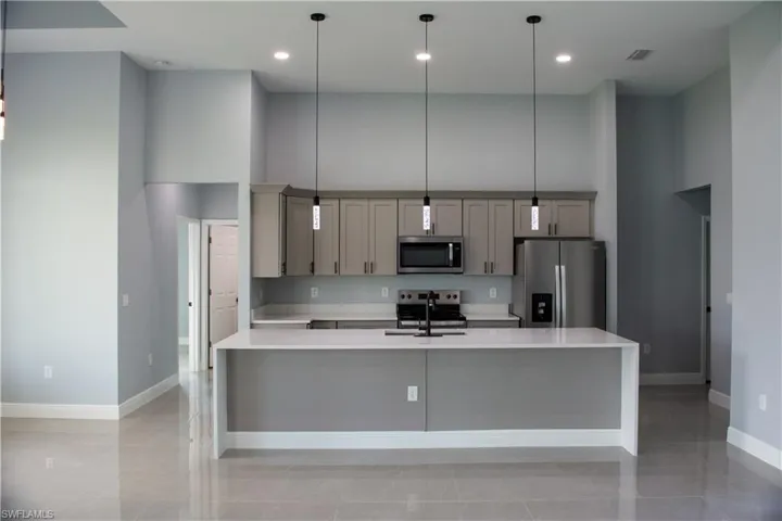 Kitchen featuring pendant lighting, a kitchen island with sink, gray cabinets, stainless steel appliances, and a high ceiling