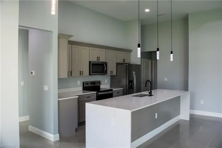 Kitchen with sink, decorative light fixtures, a center island with sink, gray cabinets, and appliances with stainless steel finishes