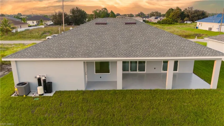 Back house at dusk with a lawn, a patio, and cooling unit