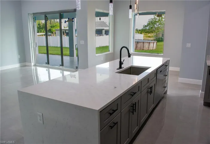 Kitchen featuring a center island with sink, sink, light stone counters, and tile patterned floors