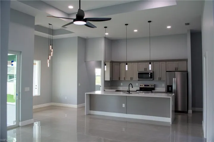 Kitchen with appliances with stainless steel finishes, a towering ceiling, sink, and gray cabinets