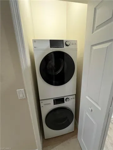 Washroom with stacked washer / dryer and light tile flooring