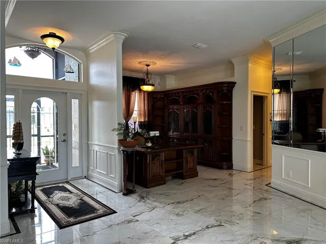Foyer with a decorative wall, marble tiled floors, wainscoting, and crown molding