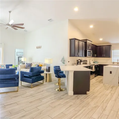 Kitchen featuring open floor plan, a breakfast bar area, stainless steel appliances, dark wood finish cabinets, and lofted ceiling