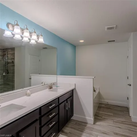 Bathroom featuring double vanity, wood finish floors, a garden tub, and tiled shower