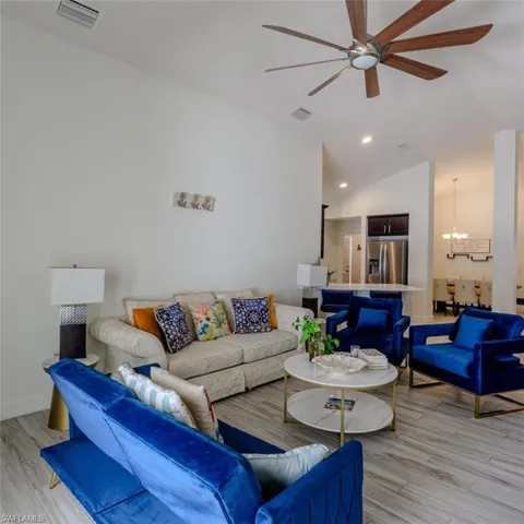 Living room with a ceiling fan, light wood-type flooring, suspended lighting, and lofted ceiling