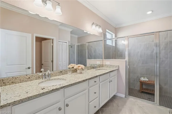 Bathroom with double vanity, a shower stall, light tile patterned flooring, and ornamental molding
