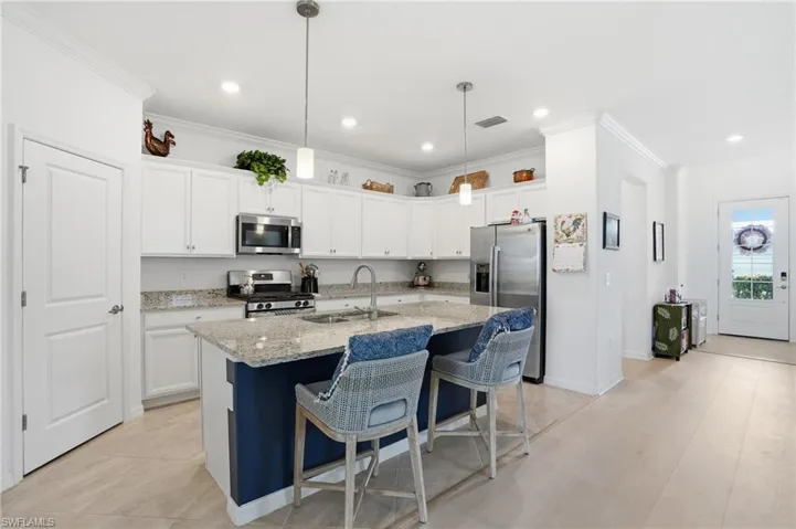 Kitchen with a kitchen bar, stainless steel appliances, white cabinets, light stone counters, and crown molding
