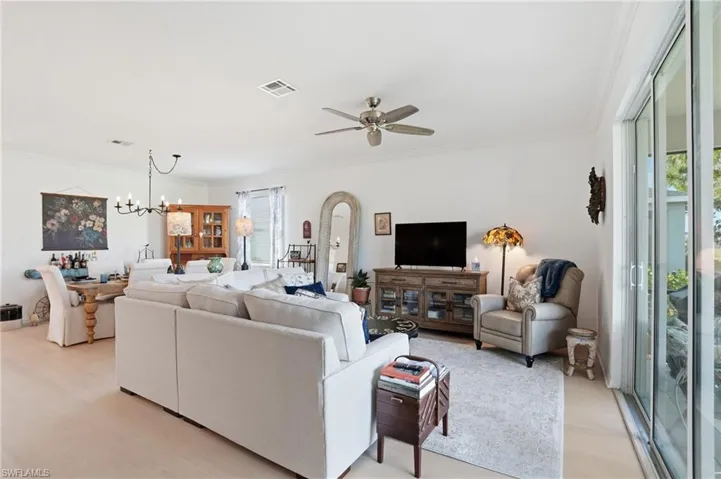 Living area featuring crown molding, a chandelier, a ceiling fan, arched walkways, and light wood-style flooring