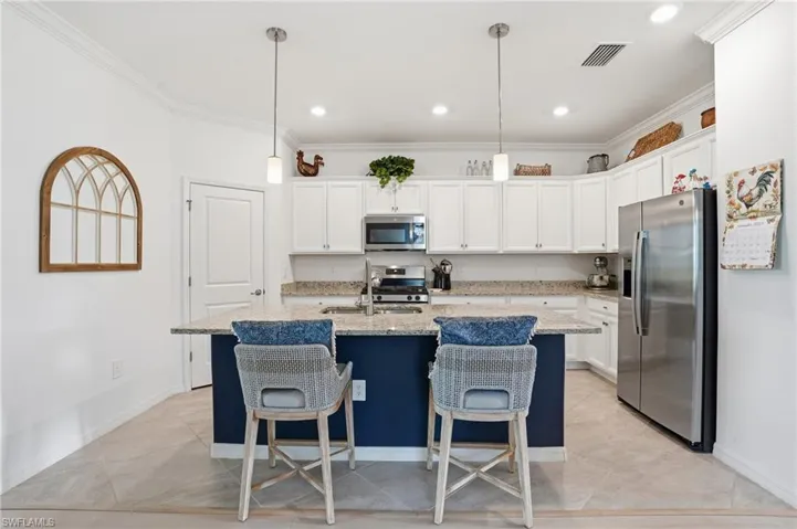 Kitchen with stainless steel appliances, ornamental molding, a center island with sink, a kitchen bar, and light stone countertops