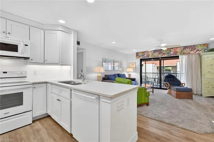 Kitchen with white appliances, open floor plan, light stone counters, tasteful backsplash, and white cabinets