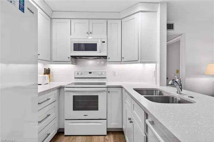 Kitchen featuring white appliances, light stone countertops, and white cabinetry