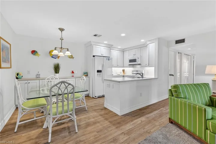 Kitchen featuring white appliances, light countertops, decorative light fixtures, white cabinets, and a peninsula