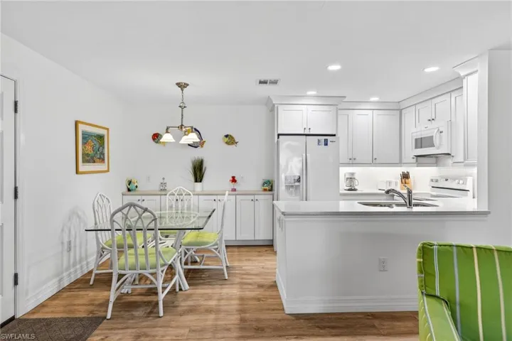 Kitchen featuring white appliances, white cabinets, decorative light fixtures, a peninsula, and light stone countertops