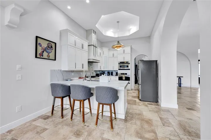 Kitchen featuring arched walkways, a breakfast bar, decorative backsplash, a peninsula, and white cabinets