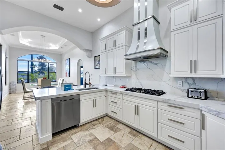 Kitchen with a raised ceiling, light stone counters, white cabinets, dishwasher, and a peninsula
