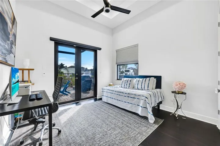 Bedroom featuring an office area, a high ceiling, french doors, dark wood-style floors, and a ceiling fan