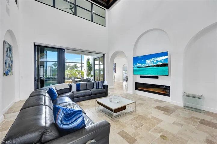 Living area with stone tile flooring, a glass covered fireplace, arched walkways, and a high ceiling