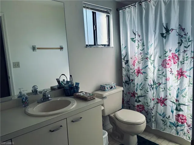 Bathroom with curtained shower, tile patterned flooring, toilet, and vanity