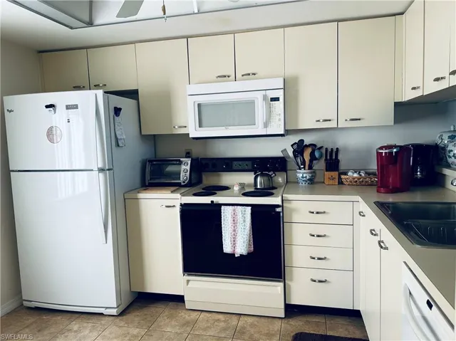 Kitchen with white appliances, light tile patterned floors, white cabinetry, and sink