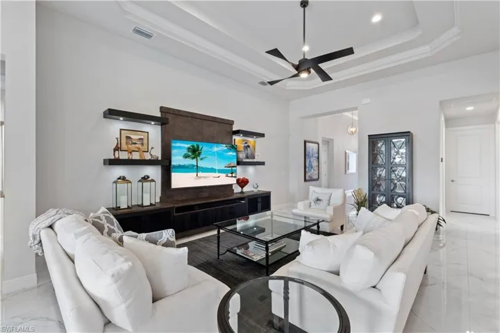 Living room with light tile patterned flooring, ceiling fan, and a tray ceiling