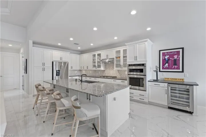 Kitchen with light tile patterned floors, beverage cooler, white cabinetry, and stainless steel appliances