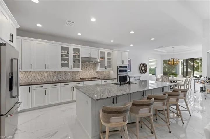 Kitchen with light tile patterned floors, white cabinets, a kitchen island with sink, hanging light fixtures, and appliances with stainless steel finishes